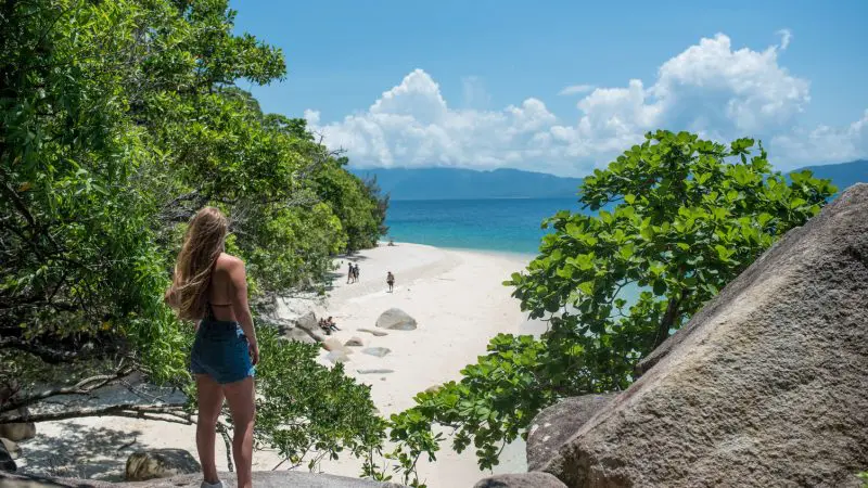 Woman standing on rocky shore gazing at Fitzroy Island, accessible via Half-day Tour Transfers with Fitzroy Island Ferries.