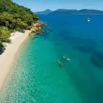 Spectacular aerial view of snorkellers exploring crystal-clear waters off Fitzroy Island’s pristine tropical beach on a half-day tour.