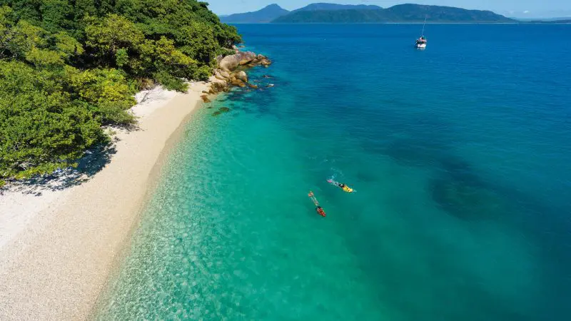 Spectacular aerial view of snorkellers exploring crystal-clear waters off Fitzroy Island’s pristine tropical beach on a half-day tour.