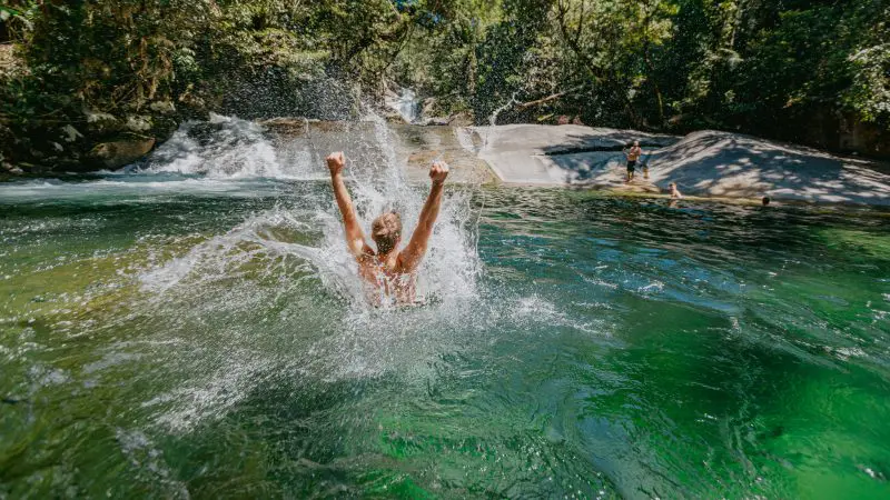 Adventurer plunging joyfully into a vibrant green river—discover this thrill on a top-rated 1 Day Waterfall and Rainforest Tour.