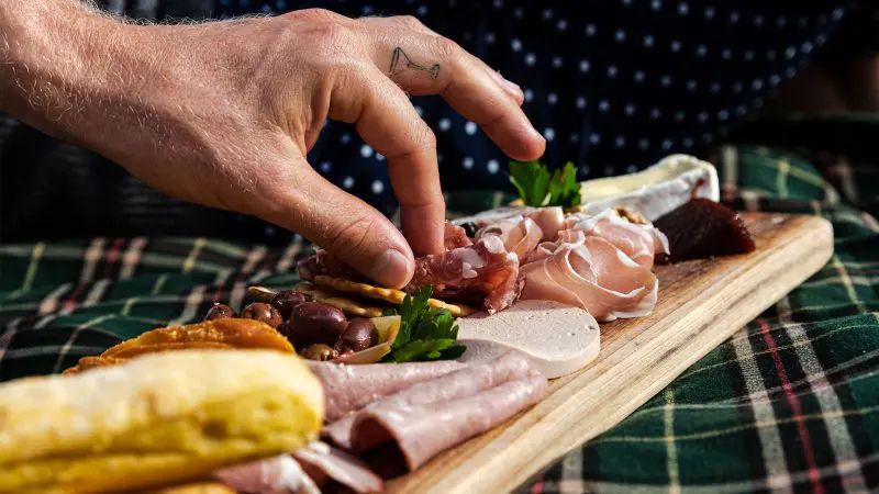 A hand picks artisan-cured meat from a gourmet charcuterie board, showcasing a premium tasting experience on Australia’s Gold Coast.
