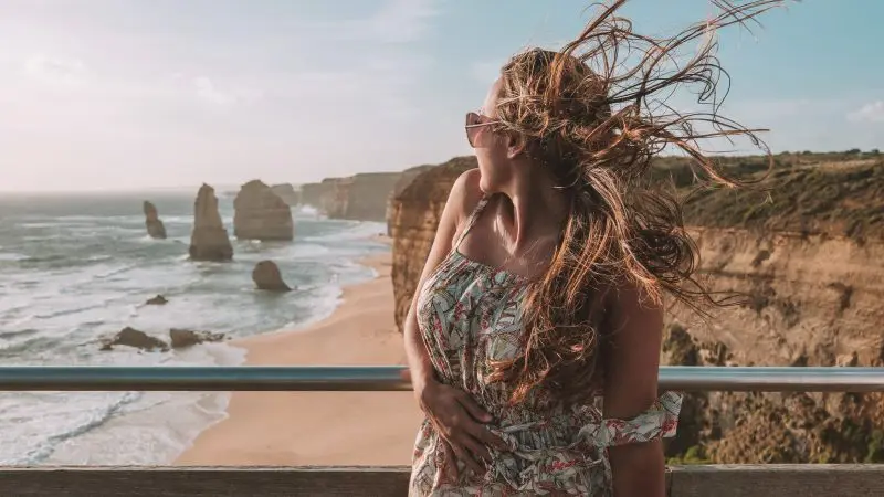 Woman with windswept hair enjoys panoramic cliff views along the Great Ocean Road during a 1 Day Reverse Eco Tour adventure.