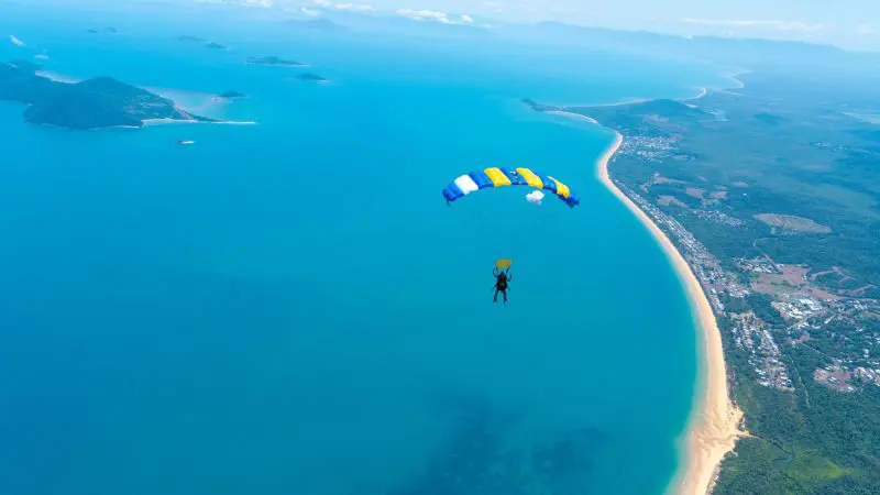 Experience breathtaking views as a skydiver with a yellow and blue parachute enjoys a 15,000ft tandem skydive over Mission Beach.