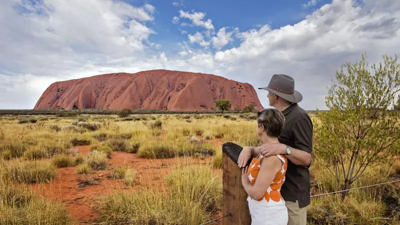 A couple admires Uluru from a fence on a 4 Day Uluru, Kata Tjuta, Kings Canyon, and West MacDonnell adventure tour in Australia.