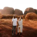 A couple holding hands among iconic Uluru Kata Tjuta desert rocks, bathed in sunlight on a 2-day tour from Ayers Rock Yulara.