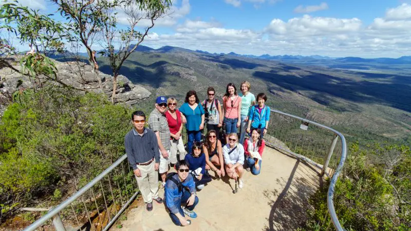 Travellers on the 3 Day Great Ocean Road Melbourne to Adelaide tour pose atop a scenic overlook with panoramic blue sky views.