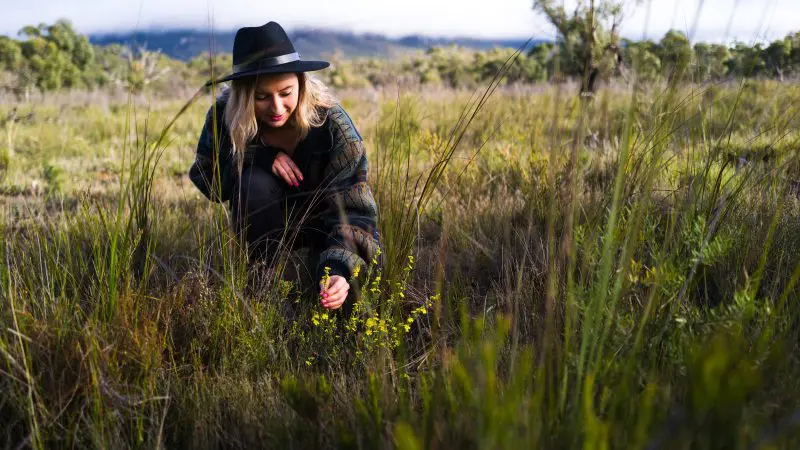Woman in a sunhat forages wild plants in lush grass during her 2 Day Great Ocean Road journey from Melbourne to Adelaide adventure.