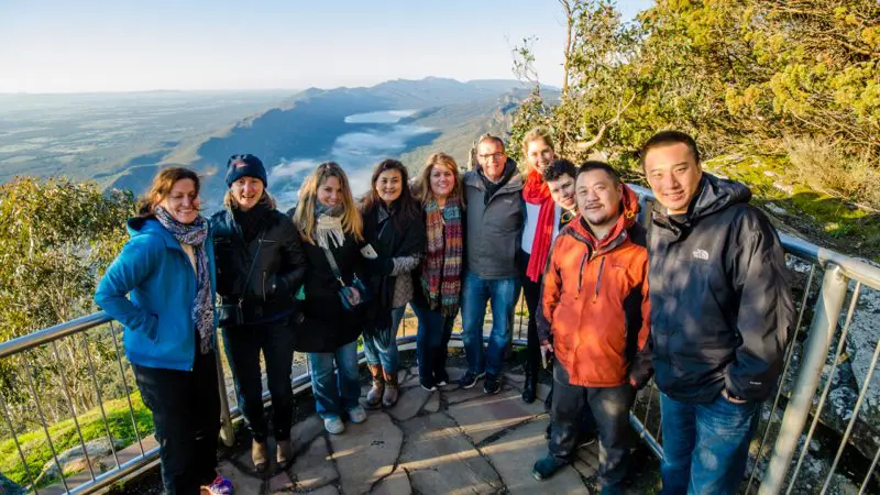 Travellers enjoying panoramic mountain vistas on the 3 Day Great Ocean Road Grampians Explorer tour from Melbourne, smiling at lookout.