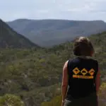 Traveller in a black "I Survived" shirt overlooks lush green hills during the 10-Day Adelaide to Perth Adventure Tour with Untamed Escapes.