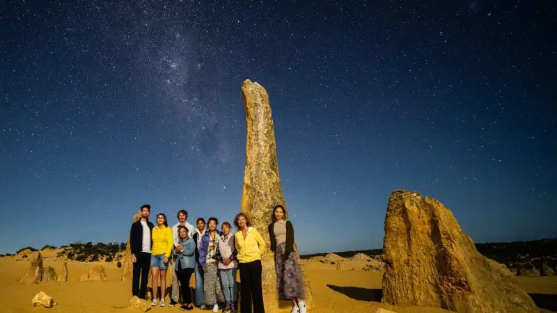Travellers on the 1 Day Pinnacles Sunset Stargazing Tour by Autopia pose at night among stunning desert rock formations under starry skies.