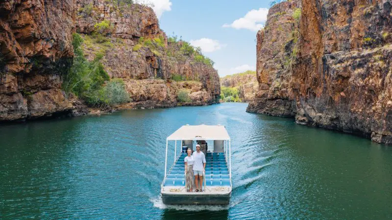 Two travellers cruise a small boat through striking red cliffs and serene waters on the ultimate 4 Day Kakadu Katherine Gorge adventure.
