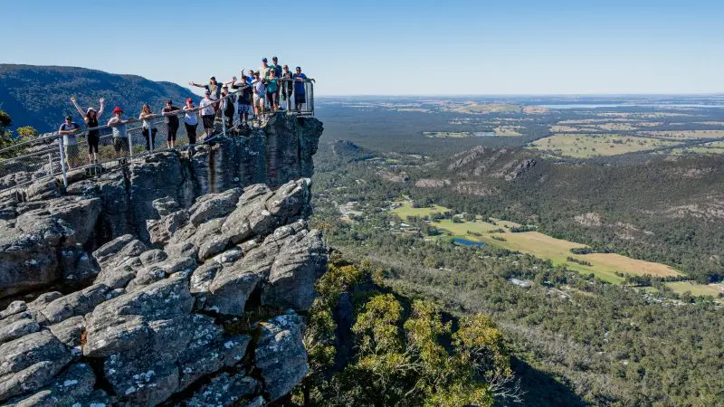 A group admires panoramic coastal views from a rocky lookout on the 3 Day Great Ocean Road Tour from Melbourne to Adelaide.