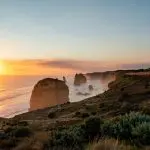 Stunning sunset illuminates rugged ocean rocks and a scenic promenade on a 1 Day Great Ocean Road Sunset Tour from Melbourne, Australia.