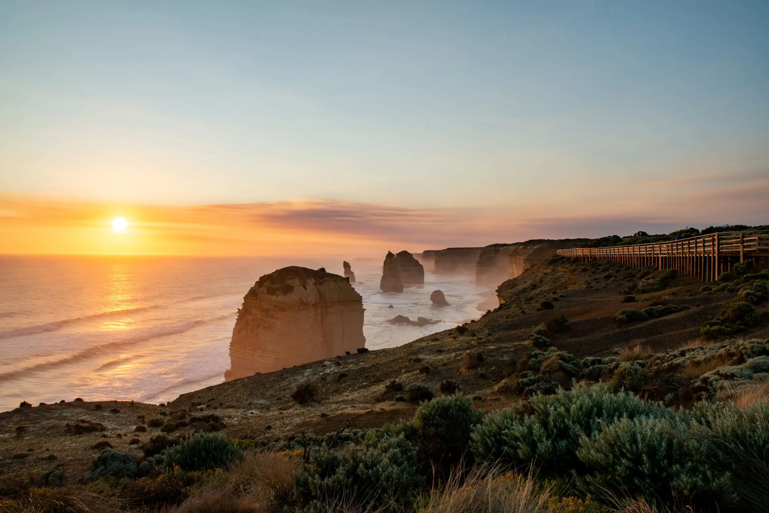Stunning sunset illuminates rugged ocean rocks and a scenic promenade on a 1 Day Great Ocean Road Sunset Tour from Melbourne, Australia.