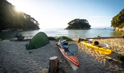Kayaks and a green tent rest on a pristine sandy beach beside tranquil waters and scenic islands—ideal for a Three Day Classic adventure.