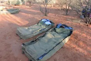 Image of Two green swag sleeping bags lie on rich red earth, showcasing a genuine 2 Day Red Centre Rock Tour adventure from Alice Springs.