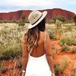 Woman in white dress and hat standing before iconic Uluru during a 3-Day Red Centre Kings Canyon Safari from Alice Springs, Australia.