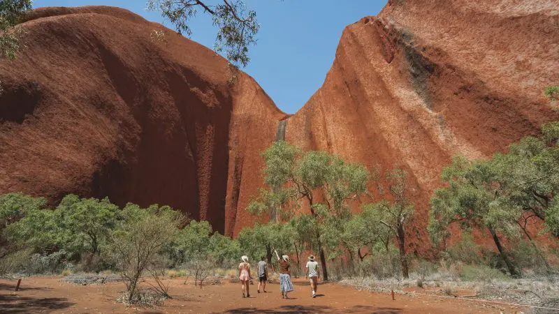 Tour group approaches iconic red rock formations during a 2-day Uluru Kata Tjuta tour from Ayers Rock Yulara, Australia.