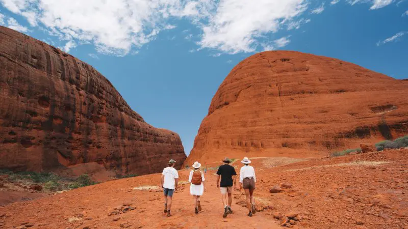 Visitors hike between stunning red rock formations under a clear sky on a 2 Day Uluru Kata Tjuta Tour departing from Ayers Rock Yulara.