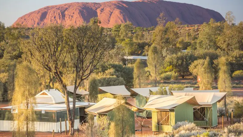 Luxury tented cabins blend seamlessly among lush trees, boasting iconic Uluru views—ideal for your 4 Day Uluru to Alice Springs tour.