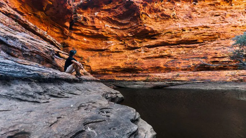 Traveller relaxes on a rocky ledge by a tranquil pool during the 3 Day Red Centre Uluru & Kings Canyon Safari tour from Alice Springs.
