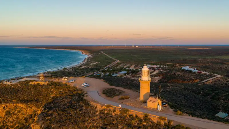 Iconic lighthouse perched on a coastal hill at sunset, overlooking the sea—top attraction on the 7 Day Perth to Exmouth Ningaloo Reef tour.