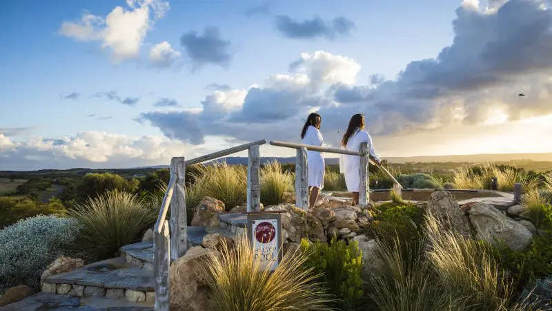 Two women in white robes relax at sunset near their Peninsula Hot Springs Spa Shuttle Bus, capturing a tranquil wellness retreat moment.