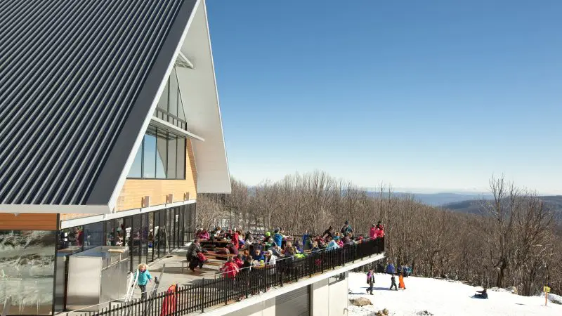 Group of skiers relaxing on a sunlit lodge terrace during a top-rated 1 Day Lake Mountain Snow Waterfalls Tour from Melbourne.
