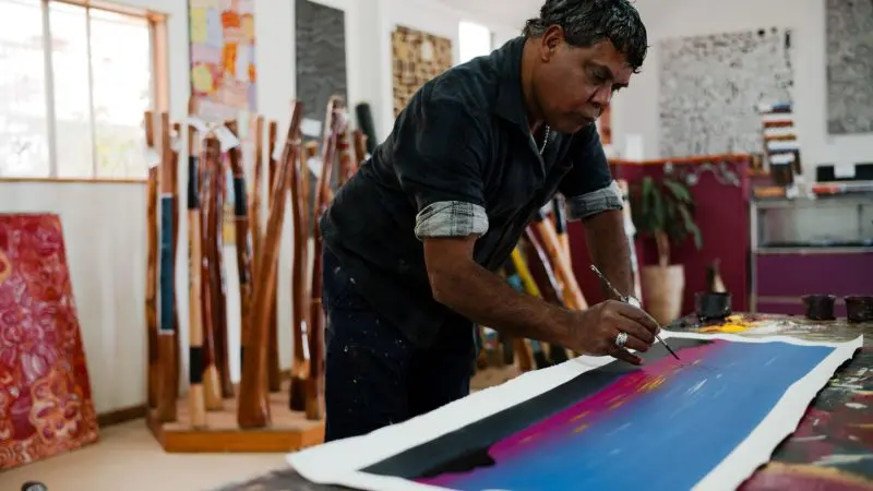 An artist paints a vibrant canvas in a studio, inspired by the 7 Day Uluru to Adelaide Experience with Untamed Escapes adventure tour.