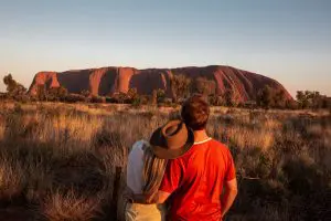 Couple gazes at Uluru during a stunning sunset on a 7-day Adelaide to Uluru Adventure by Untamed Escapes, Australia tour.
