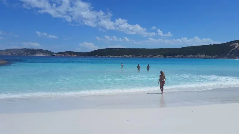 Woman on pristine white sand during 10 Day Perth to Adelaide Adventure Tour by Untamed Escapes; others enjoy crystal-clear blue water.