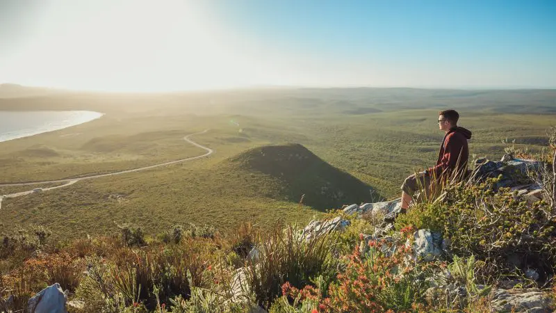 Traveller soaking in panoramic, sunlit vistas from a rocky hill on the 10 Day Perth to Adelaide Adventure Tour by Untamed Escapes.