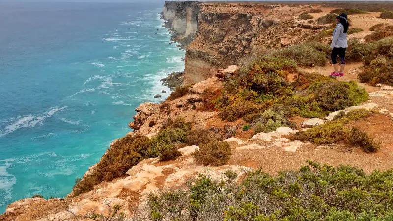 Traveller on rocky cliff edge overlooks breathtaking coastal scenery during the 10 Day Perth to Adelaide Adventure Tour Untamed Escapes.