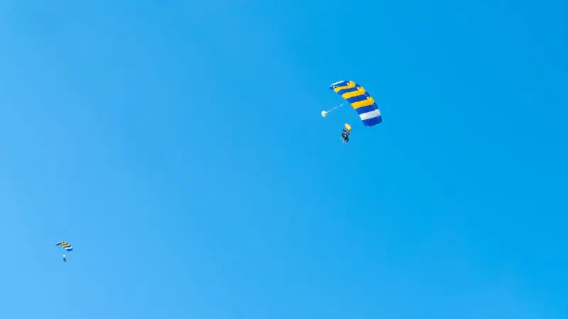 Skydivers with vibrant striped parachutes glide over Wollongong in a tandem skydive from 15,000 feet beneath a clear blue sky.