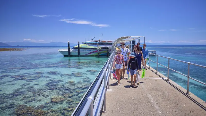 Travellers stroll along a scenic pier above crystal-clear blue waters under the sun, departing for Green Island’s 9am Half-Day Tour.