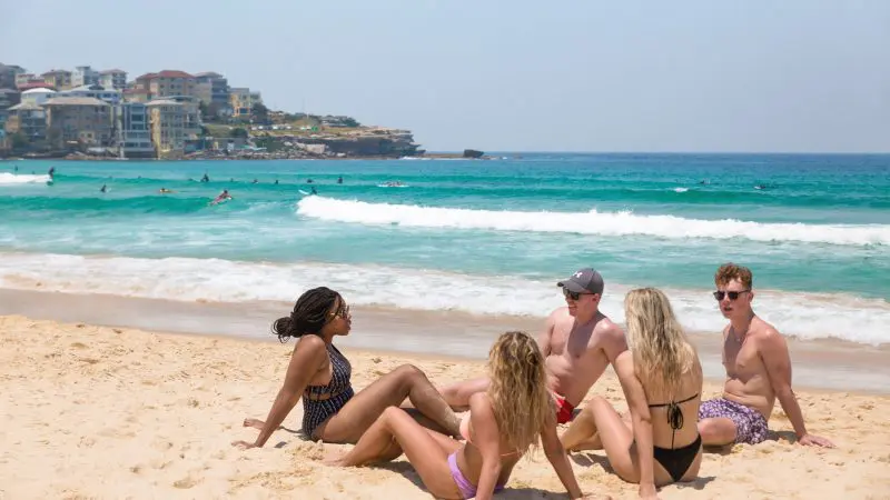 Four travellers relax on the sunlit sand, enjoying friendly conversation during a 10 Day Oz Intro Sydney to Brisbane group tour adventure.