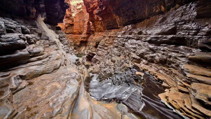 Spectacular narrow rocky gorge with striking layered stone cliffs and a clear stream, featured on a 10-Day Perth to Broome tour.