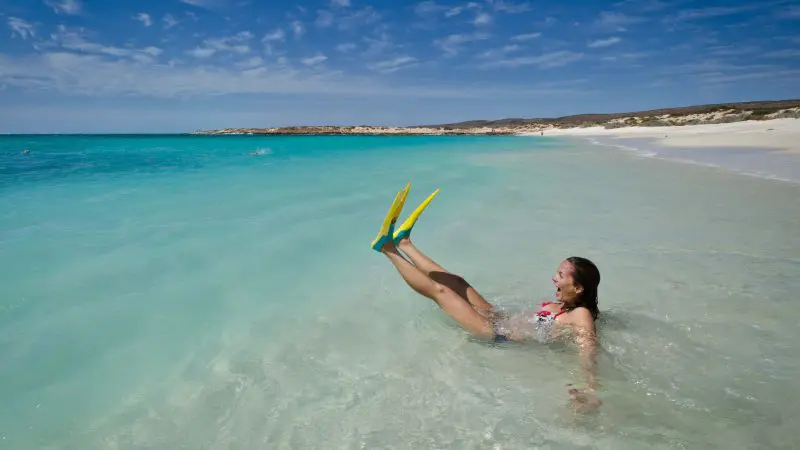 A woman in vibrant yellow flippers relaxes in clear turquoise shallows on a 10 Day Perth to Broome West Coast Adventure tour.