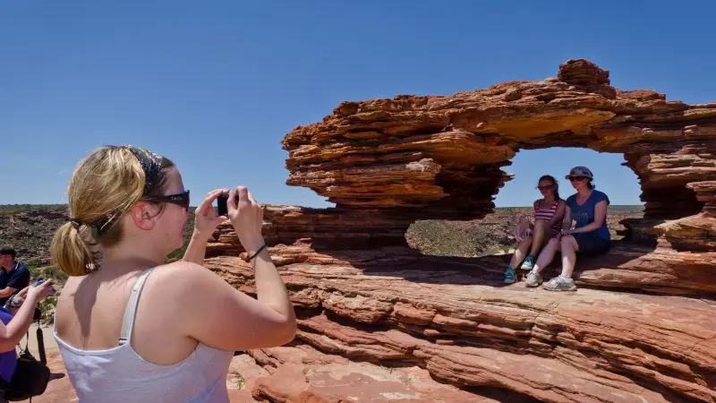 A woman takes photos of two travellers atop stunning red rocks during their epic Perth to Darwin adventure holiday tour package.