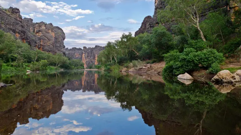 Experience a tranquil river mirroring rugged cliffs and lush trees—iconic landscape on a 10 Day Darwin to Broome 4WD Adventure tour.