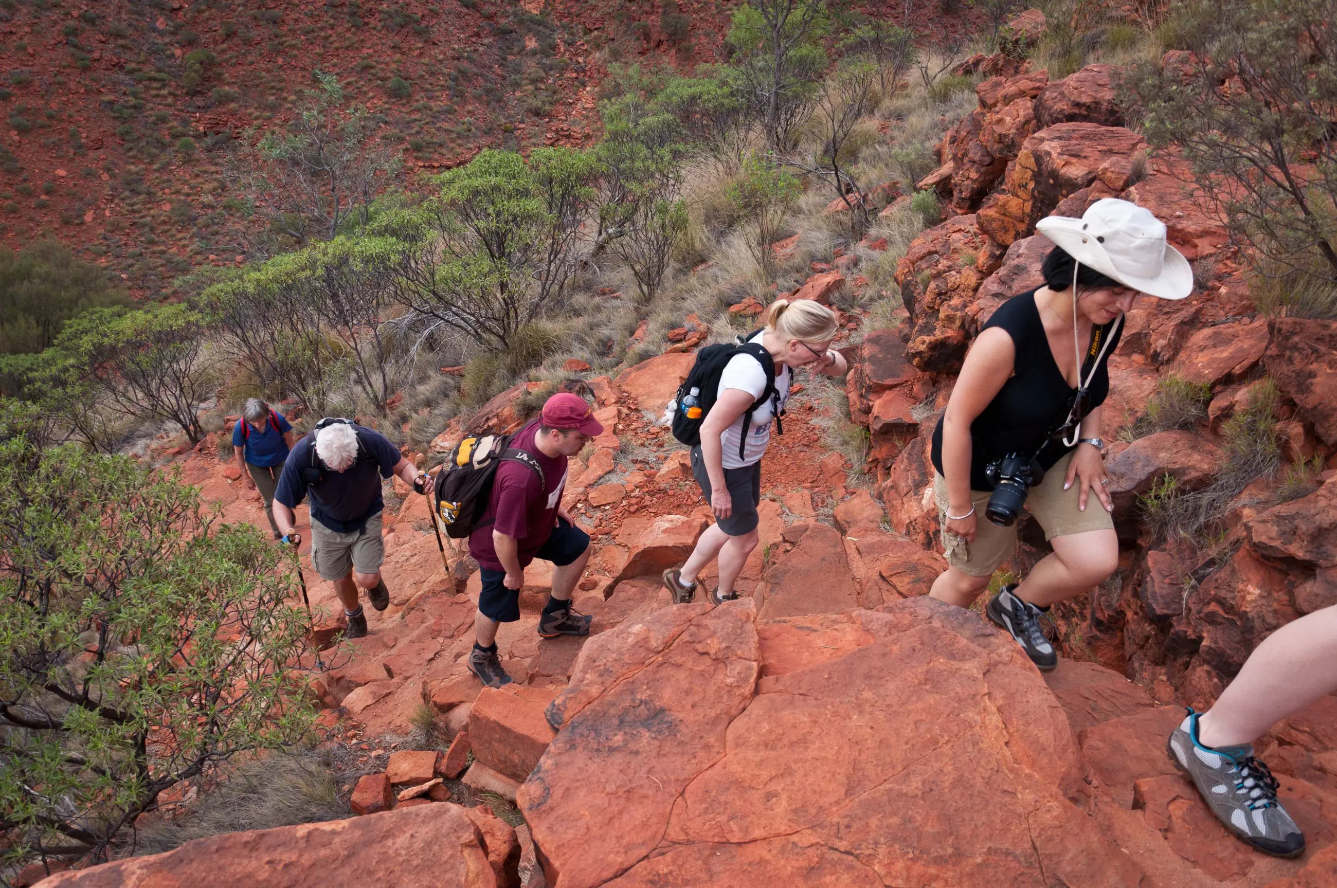 Five hikers trek a rugged, red-rock trail on a five-day Outback camping adventure loop from Alice Springs, Australia.
