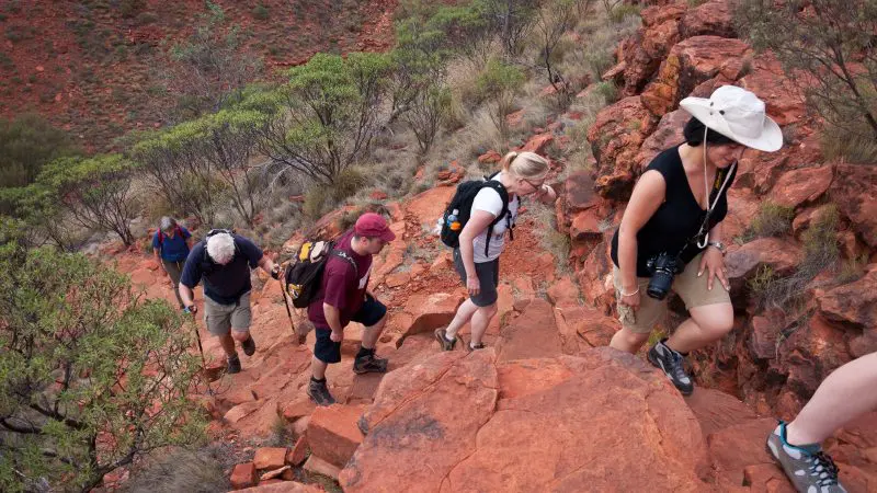 Five hikers trek a rugged, red-rock trail on a five-day Outback camping adventure loop from Alice Springs, Australia.