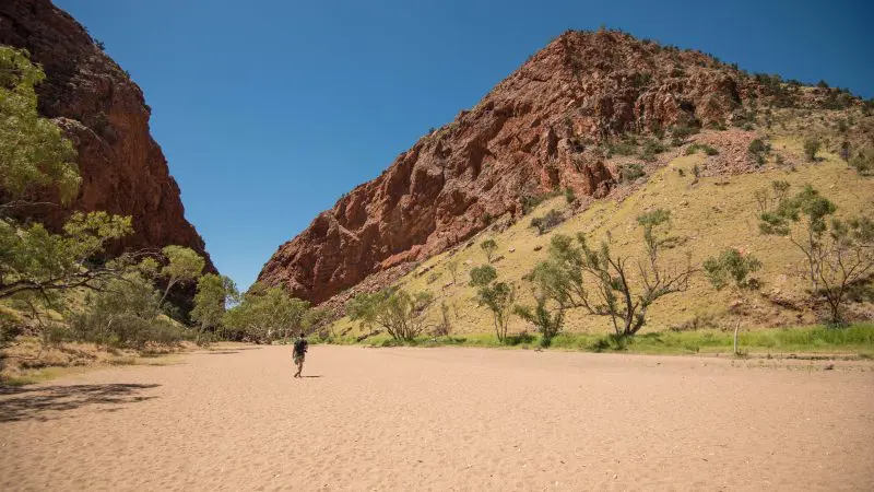 Traveller on sandy trail winding through rugged rocky hills during a 2-night MacDonnell Ranges tour from Alice Springs, Australia.