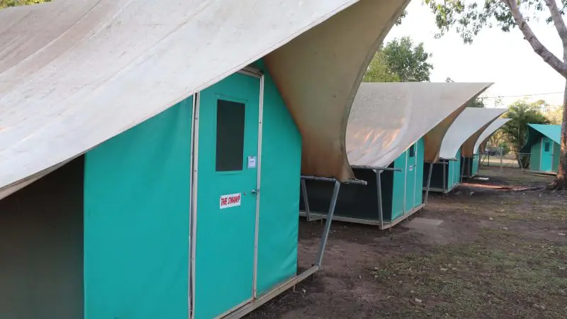Discover a row of green canvas-roofed tents for Kakadu Tour Camping, set beneath shady trees in a scenic, natural outdoor setting.