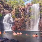 Visitors enjoy swimming in a crystal-clear natural pool at Twin Waterfalls, Kakadu, encircled by dramatic cliffs and verdant rainforest.