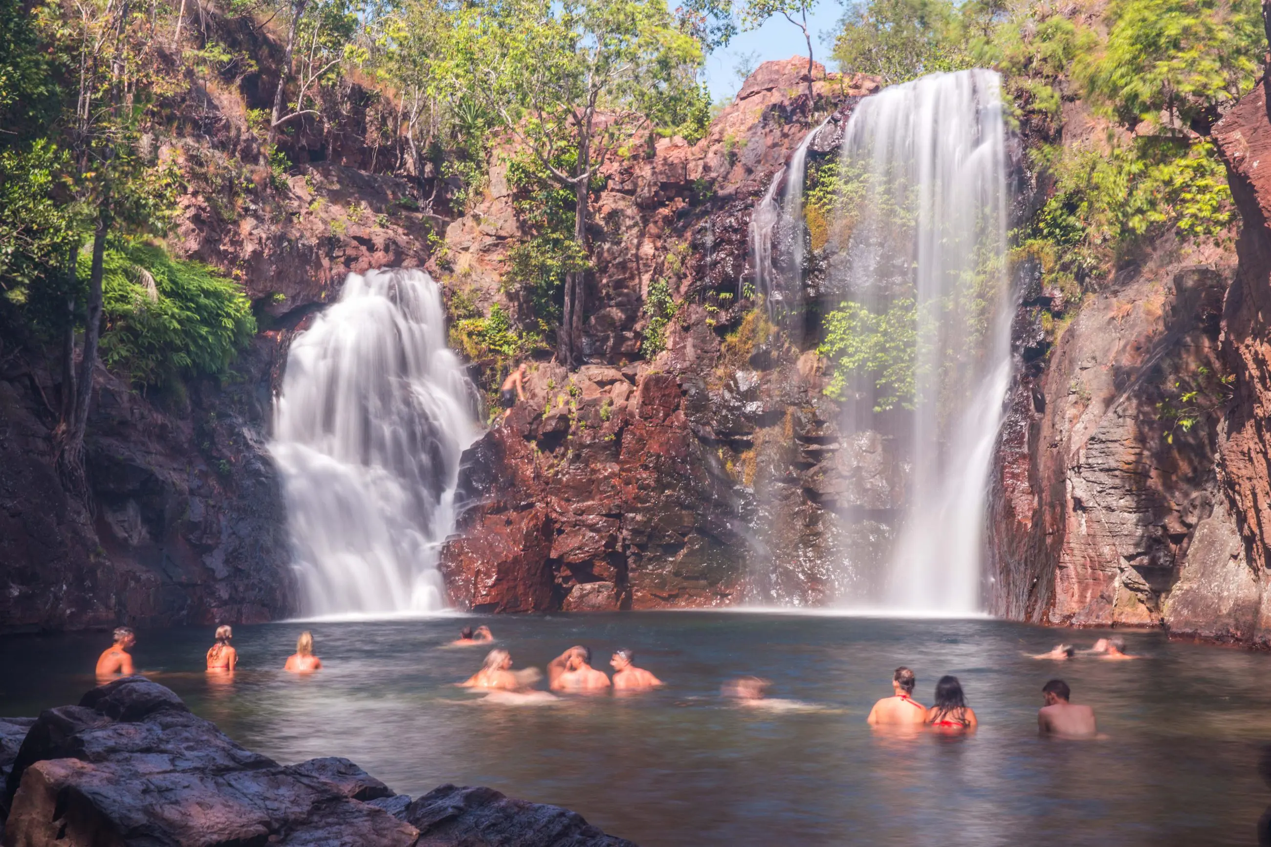 Visitors enjoy swimming in a crystal-clear natural pool at Twin Waterfalls, Kakadu, encircled by dramatic cliffs and verdant rainforest.