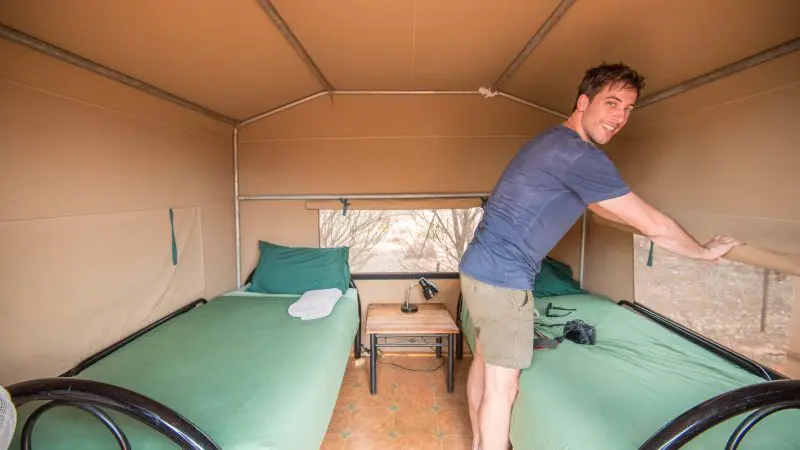 Happy traveller inside a canvas tent on a 3 Day Uluru Adventure from Alice Springs, lifting tent flap to take in scenic outback views.