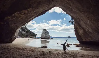 A joyful person stands on a sandy beach, arms raised towards the sky, enjoying a vibrant sea view and sunny coastal atmosphere.