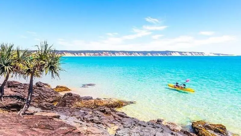Adventurer kayaking on vibrant turquoise water by rugged Noosa coastline during a Dolphin Sea Kayak Beach 4x4 Tour, Queensland.