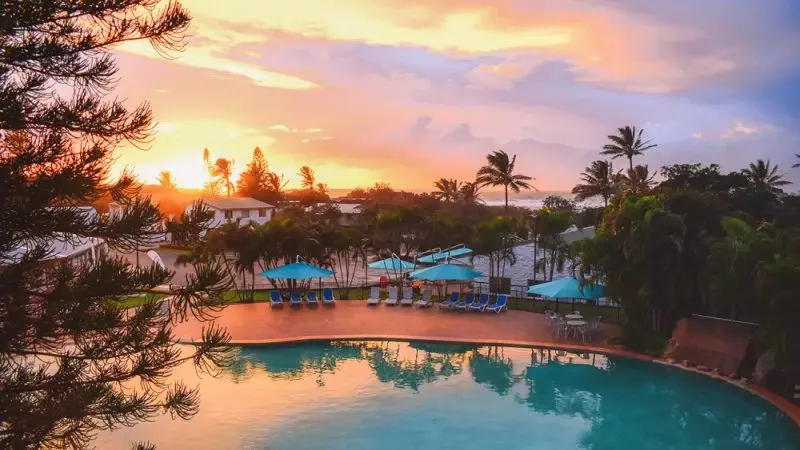 Luxury swimming pool with loungers and parasols at sunset, ideal for relaxing after a Kgari 2 Day Tour Ex Hervey Bay experience.